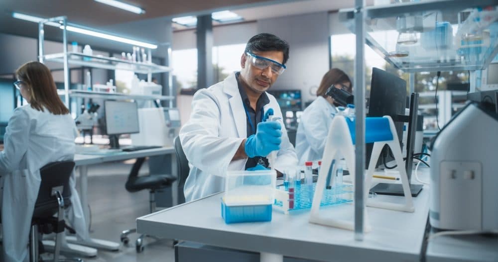 A laboratory technician pipetting samples into tube racks in an analytical microbiology laboratory.